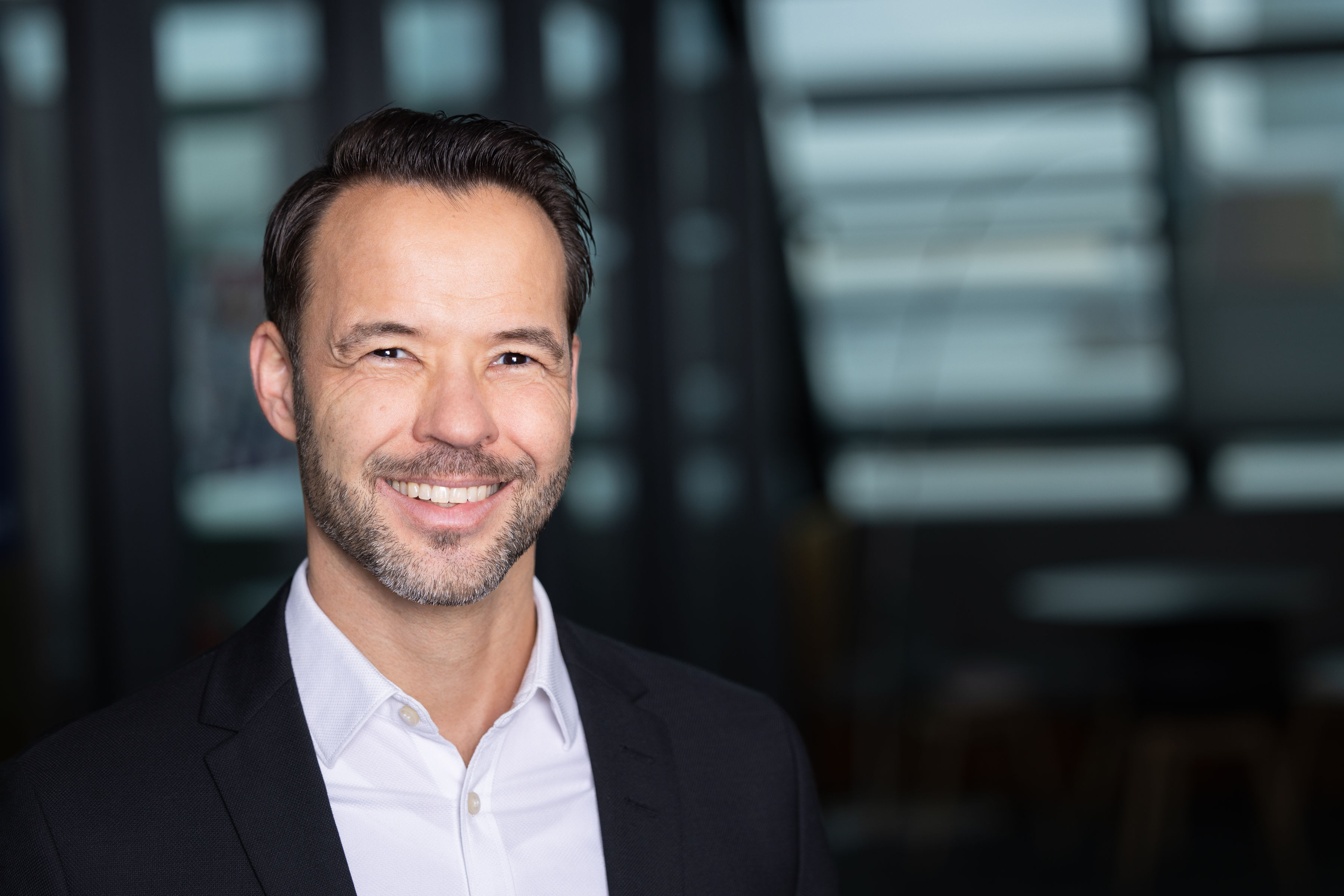 ein lächelnder Mann in einem dunklen Anzug und weißem Hemd