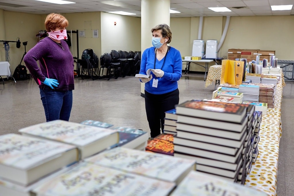 Two Mars Associates from AMERICAN HERITAGE® Chocolate wearing masks beside donated books.