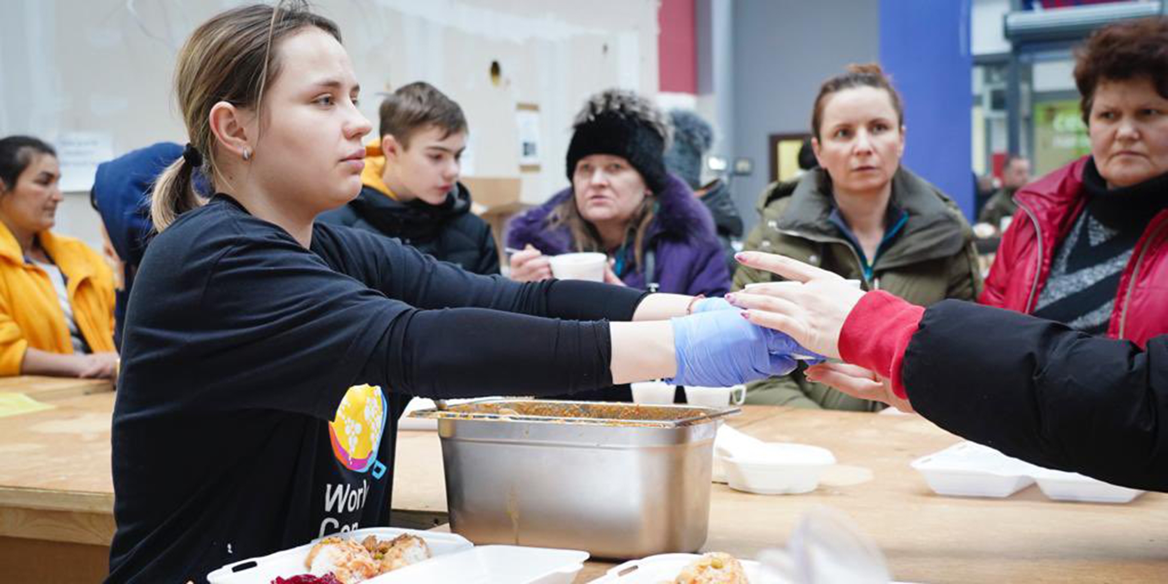 Young woman handing food to another person at a soup kitchen