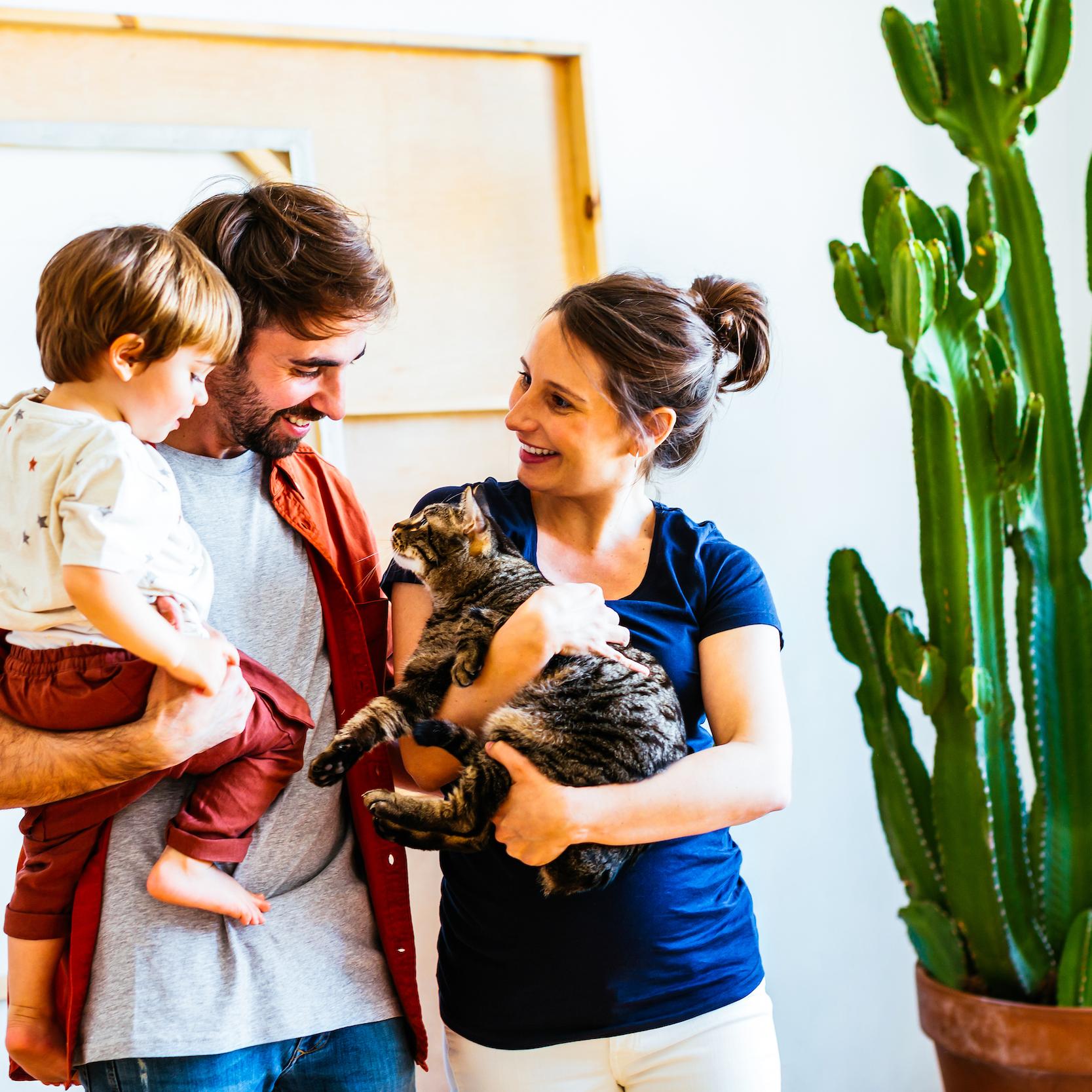 Smiling parents with child and a cat, standing next to a cactus