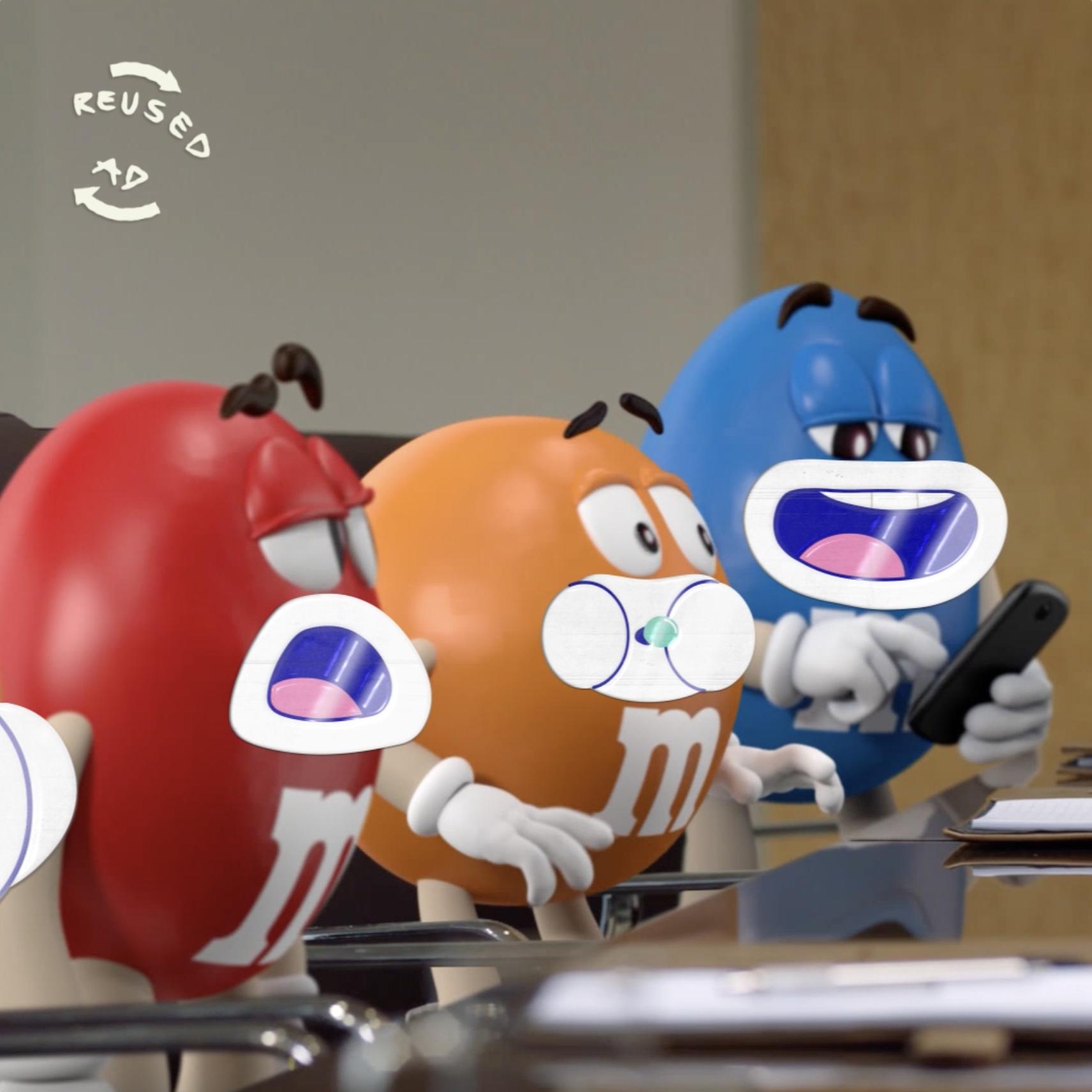 Yellow, Red, Orange, and Blue M&M sat at a table. Blue is looking at his phone. Reused ad logo.]