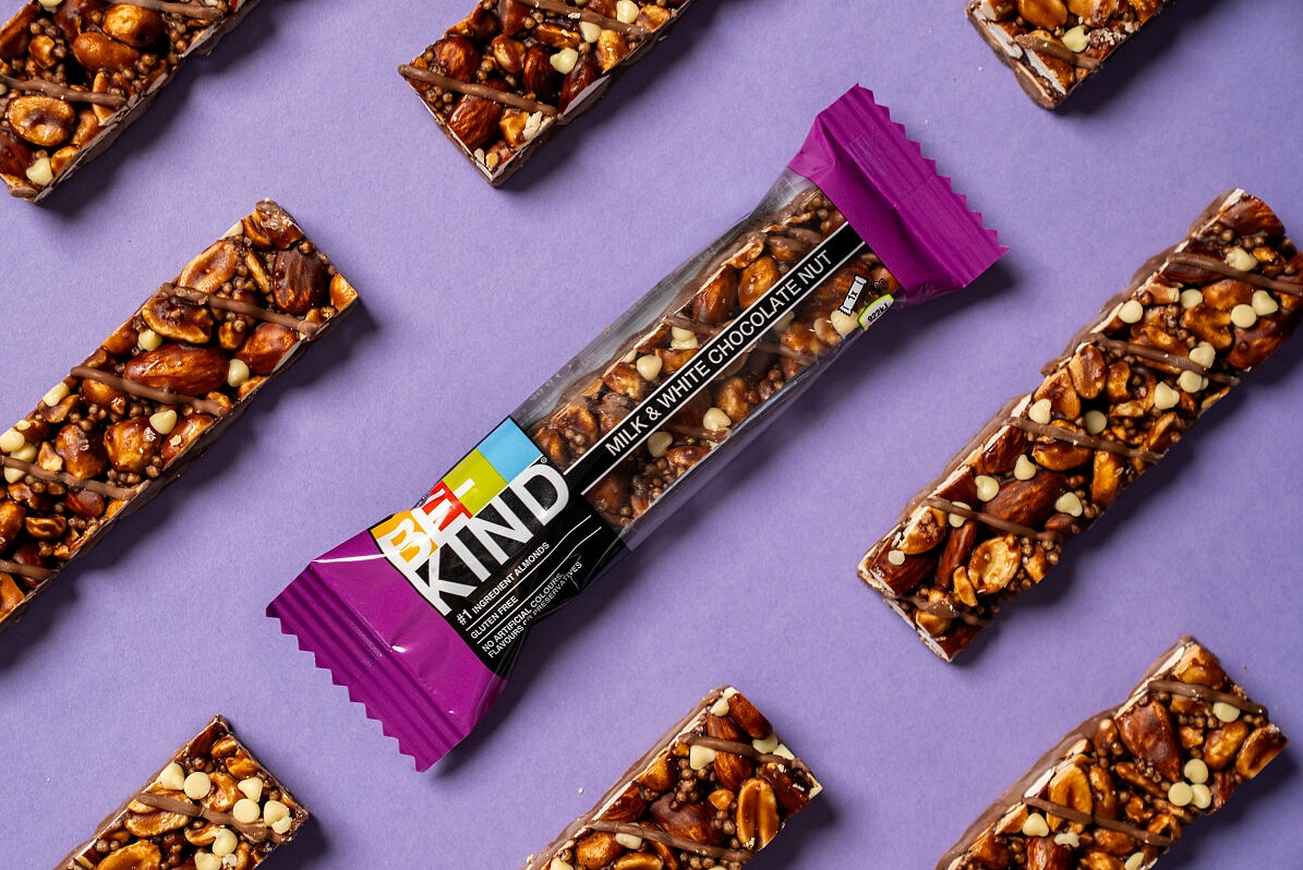 Mehrere BE-KIND Milk & White Chocolate Nut Riegel vor einem lila Hintergrund