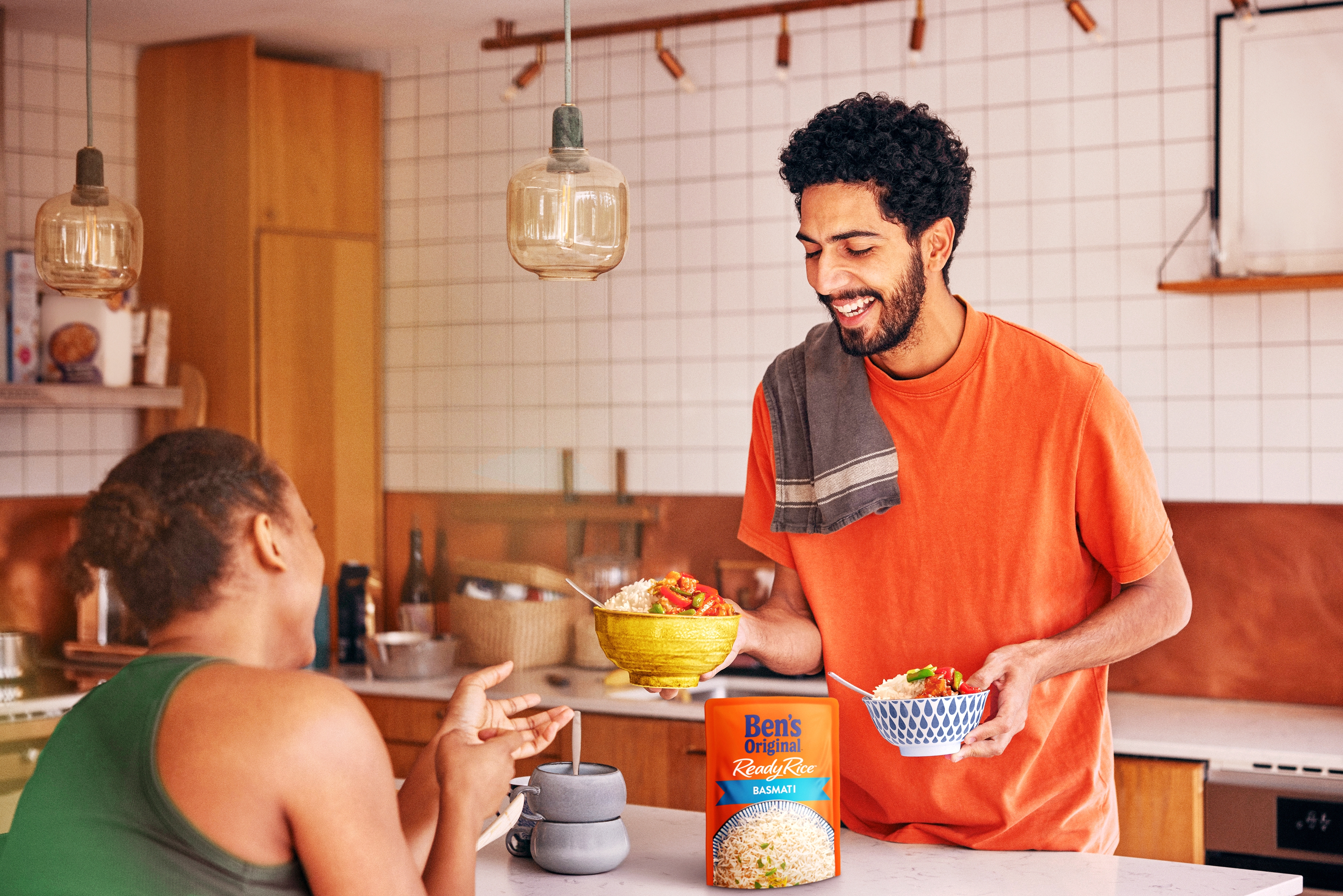 A man smiles while handing a woman a bowl of Ben's Original rice in a kitchen.