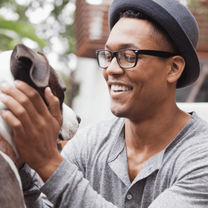 A man kneeling down smiling and petting his dog.