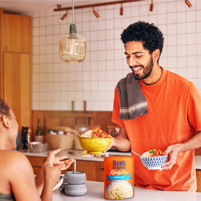 A man smiles while handing a woman a bowl of Ben's Original rice in a kitchen.