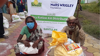 A Mars Wrigley Foundation banner stands behind people beside their large dry-ration kits.