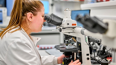 A woman examining a sample under a microscope.