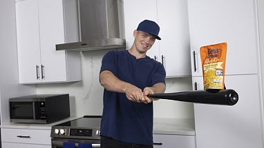 Baseball player Ben Rice poses with a baseball bat and a package of Ben's Original rice in a kitchen