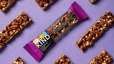 Mehrere BE-KIND Milk & White Chocolate Nut Riegel vor einem lila Hintergrund