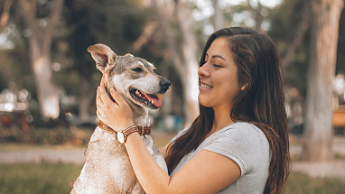 A woman lovingly holding a dog outside in the grass.
