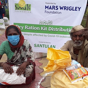 A Mars Wrigley Foundation banner stands behind people beside their large dry-ration kits.