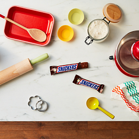 Snickers bars on a kitchen counter with baking utensils and ingredients