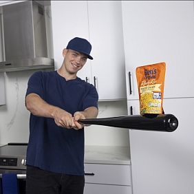 Baseball player Ben Rice poses with a baseball bat and a package of Ben's Original rice in a kitchen