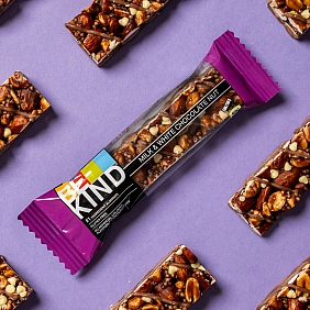 Mehrere BE-KIND Milk & White Chocolate Nut Riegel vor einem lila Hintergrund