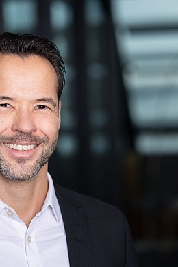 ein lächelnder Mann in einem dunklen Anzug und weißem Hemd