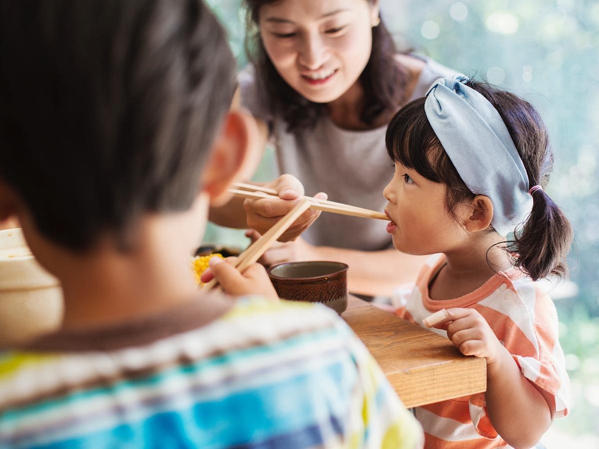 A family sitting around their dinner table with chopsticks in their hands right before mealtime.